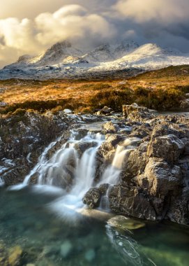 Breathtaking Winter view of the Cuillin mountain range covered in snow on the Isle of Skye, Scotland. A small waterfall can be seen in the foreground, located not far from the famous Sligachan bridge! clipart