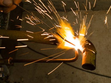 Bir metal parçasını kıvılcımlar ve argon kaynaklarıyla kaynak yapan biri..