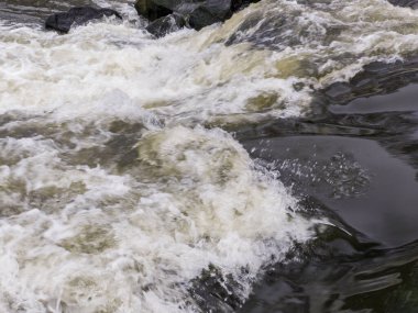 Arkasında kayalar olan büyük bir su kütlesi..