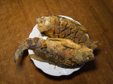 Çıtır çıtır, baharatlı derisi beyaz bir tabakta sunulmuş iki kızarmış balık. Sıcak ahşap arka plan iştah açıcı dokuyu ve zengin rengi arttırır. Yemek fotoğrafçılığı, ev yemeği pişirme ilhamı ve yemek hazırlama kavramları için idealdir. Tam oldu.