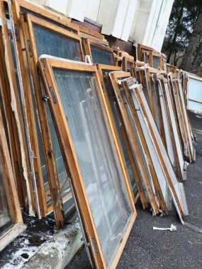 Çöpe atılmış ahşap pencere çerçeveleri, yıpranma ve yaşlanma belirtileri gösteriyor, bir binanın ön cephesine yaslanıyor. Yerdeki kar ve buz soğuk bir kış ortamını işaret ediyor. İnşaat, yenileme veya çevre dostu yapı temaları için ideal.