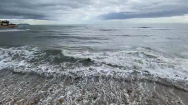 Denizin üzerinde fırtına bulutları ve kumsalda dalgalar.