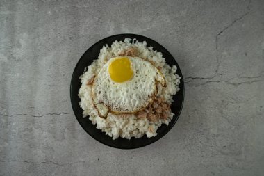 Pişmiş pirinçli siyah tabak, kızarmış yumurta ve ton balığı masada. yiyecek