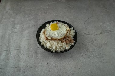 Pişmiş pirinçli siyah tabak, kızarmış yumurta ve ton balığı masada. yiyecek