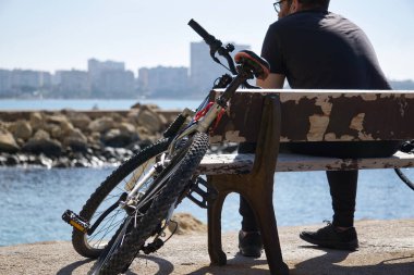 İspanya 'nın Valensiyalı Topluluğu' nda Alicante şehrinin kıyısında bisikletiyle denize bakan bir çocuk. görünüm