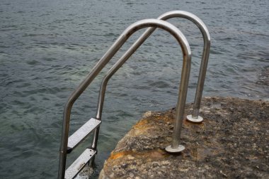 İspanya 'nın Alicante eyaletindeki Moraira kasabasının kıyısındaki sahildeki kayalıklarda bulunan metal havuz merdiveni. görünüm