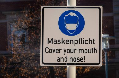İşaret levhası Almanca ve İngilizce bir maske takın
