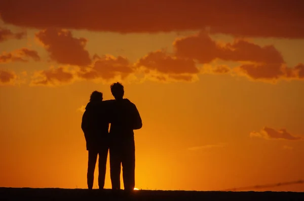 Couple devant un ciel brûlant en soirée d'été. Silhouettes dans la lumière du soir — Photo