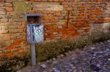 Eski, yıpranmış tuğla duvarın önündeki çöp tenekesi.