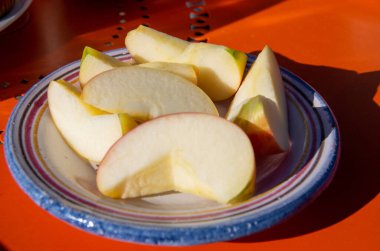 Güneşte kırmızı masada dilimlenmiş elmalı küçük tabak.