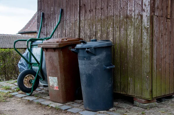 Çöp tenekesi ve el arabası ahşap bir kulübeye yaslanıyor.
