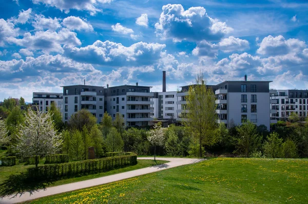 Ön planda ilkbahar çayırı ve bulutlu bahar gökyüzü olan modern apartmanlar.