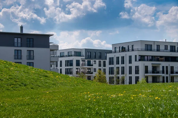 Ön planda ilkbahar çayırı ve bulutlu bahar gökyüzü olan modern apartmanlar.