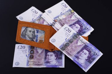 Üzerinde para olan sarı deri bir cüzdan koyu bir arka planda duruyor.