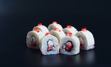 Deniz ürünleri ve balıklı renkli japon dürümleri koyu bir arka planda yatar.