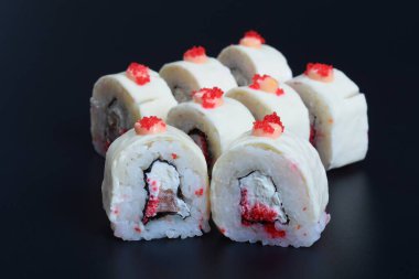 Deniz ürünleri ve balıklı renkli japon dürümleri koyu bir arka planda yatar.