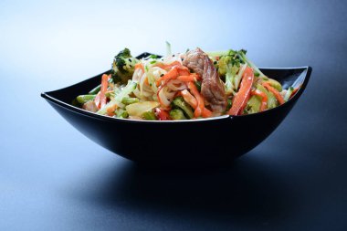 Et, sebze ve soslu sıcak salata koyu bir tabakta.