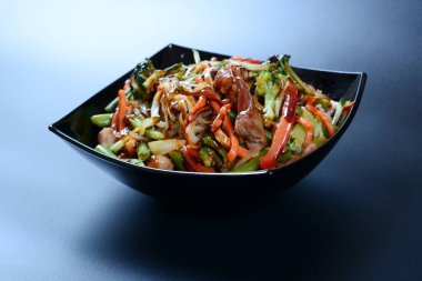 Et, sebze ve soslu sıcak salata koyu bir tabakta.