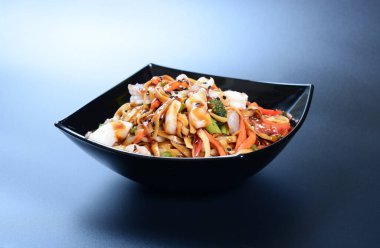 Karides, sebze, deniz ürünü ve soslu sıcak salata koyu bir tabakta.