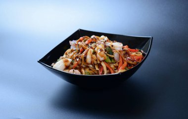 Karides, sebze, deniz ürünü ve soslu sıcak salata koyu bir tabakta.