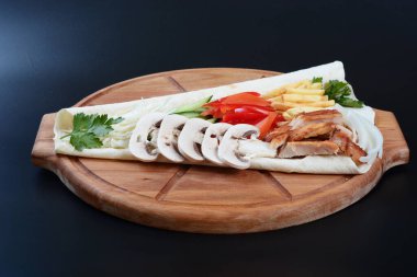 Domatesli, salatalıklı, etli ve otlu tortilla koyu bir arka planda yatıyor.