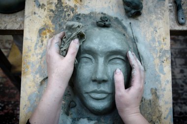 The blank plasticine mask is in the hands of the sculptor clipart