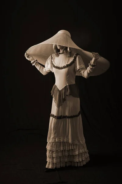 一个穿着旧衣服戴旧帽子的女孩站在黑暗的背景上 很伤心 — 图库照片