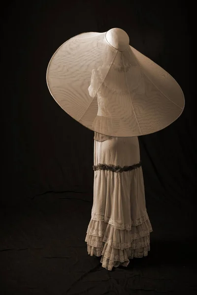 一个穿着旧衣服戴旧帽子的女孩站在黑暗的背景上 很伤心 — 图库照片