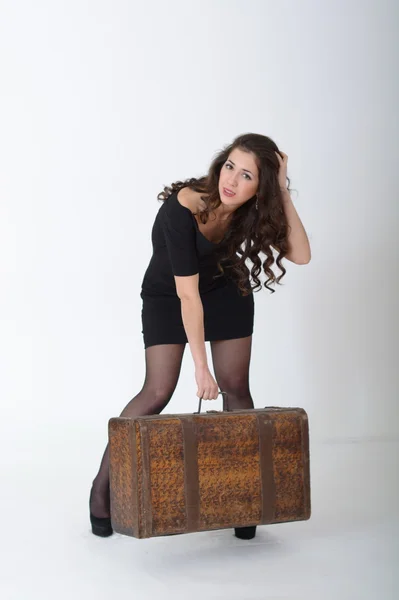 Una ragazza bruna si erge con valigia antica su sfondo bianco — Foto Stock