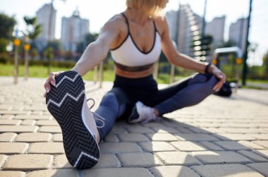 Genç sporcu kadın esniyor ve koşmaya hazırlanıyor. Spor kıyafetli spor kadın şehir caddesinde egzersiz yapıyor. Açık hava spor kıyafetleri ve ayakkabılar, şehir tarzı. Spor ayakkabıları yakın çekim