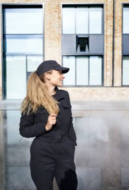 Binanın yanında iş üniformalı ve şapkalı gülümseyen bir kadının portresi. Teslimat deposunda ya da profesyonel teknik servis çalışanı gibi görünüyor. Reklam kavramı.