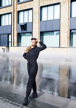 Binanın yanında iş üniformalı ve şapkalı gülümseyen bir kadının portresi. Teslimat deposunda ya da profesyonel teknik servis çalışanı gibi görünüyor. Reklam kavramı.