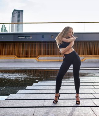 Şehir caddesinde poz veren uzun sarı saçlı güzel bir kadın dansçı. Kadın dans doğaçlaması - Latin dansı, tango, çağdaş ve bachata