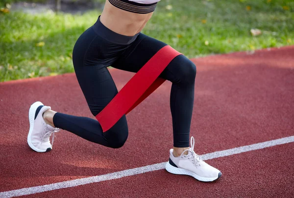 Açık havada direnç bandı fitness. Spor kıyafetleri içinde mükemmel vücudu olan genç atletik bir kadın şehir parkında lastik kayışla egzersiz yapıyor.