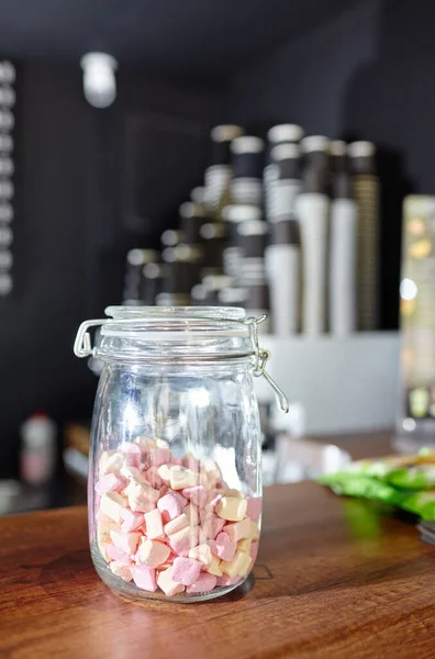 Jar with tasty mini marshmallows at bar counter in coffee shop. Blurred image, selective focus — Stock Image Jar Tasty Mini Marshmallows Bar Counter Coffee Shop Blurred Image Stock Picture