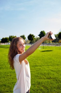 Selfie zamanı. Yazlık parkta akıllı telefonuyla selfie çeken neşeli, çekici genç bir kadın.