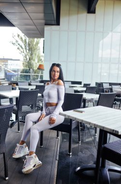 Kafede poz veren çekici fitness kadını. Spor kıyafetleri giyen sağlıklı bir kız. Güzel genç spor kadını antrenmandan sonra dinleniyor. İçecek için bekliyorum.