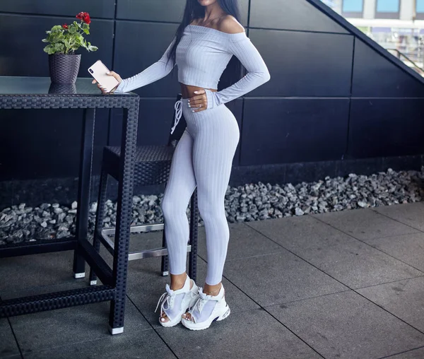 Attractive fitness woman posing in cafe. Healthy girl wearing trendy sportswear. Beautiful young sports woman relaxing and having rest after training.Waiting for beverage.Holding mobile phone