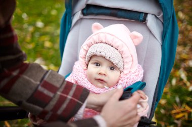 Sonbahar parkında bebek arabasında yürüyüş. Mavi sandalyede oturan, sıcak giysili sevimli küçük kız. Bebek arabasındaki çocuk