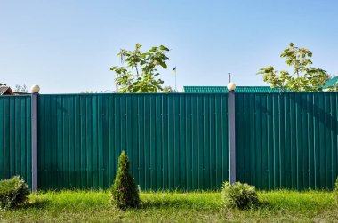 Mavi gökyüzüne karşı fenerli metal çitler. Yeşil çimenler ve küçük köknar