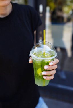 Şehir kafesinde elinde mojito olan plastik bardak tutan bir kadın. Buzlu meyve ve bitki süslemeli taze kokteyl içeceği. Seçici odak, bulanık arkaplan