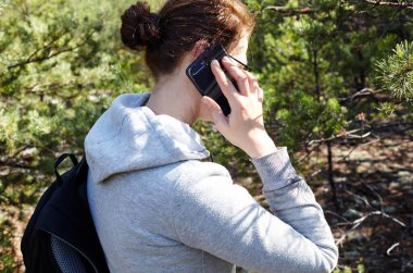 Sırt çantalı yürüyüşçü kadın sonbahar ormanında yolda yürüyor. Kadın dinlenirken cep telefonuyla konuşuyor. Gezinti ve macera