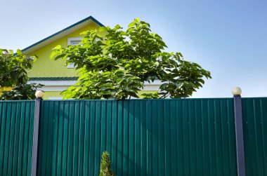 Sarı bir banliyö binasının ön cephesi. Mavi gökyüzüne karşı fenerli metal çitler.