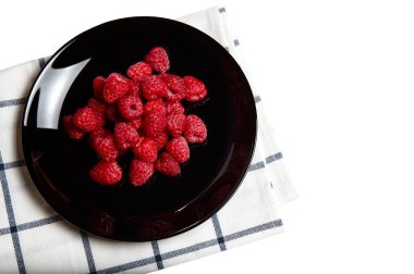 Siyah tabakta kırmızı ahududu yığını mavi şeritli havluyla beyaz arka planda, kırpma yolu ile izole edilmiş. Tasarım için, gölge yok.