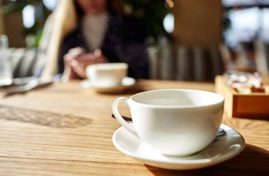 Masanın üzerinde bir fincan kahve. Bir kafede akıllı telefondan mesaj yazan bir kadın. Genç bir kadın kahve masasında cep telefonu kullanarak oturuyor. Kahve molası. Bulanık resim,