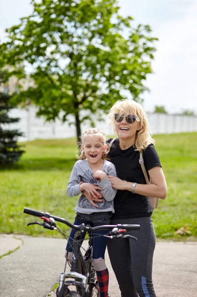 Mom and daughter have fun on the same bike and resting in nature. Adorable family ride a bike and have a good time
