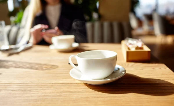 Cup of coffee on the table. Woman typing text message on smart phone in a cafe. Young woman sitting at a table with a coffee using mobile phone. Coffee break.  Blurred image,