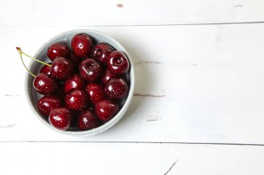Ahşap arka planda seramik bir kasede tatlı kirazlar, yakın plan. Bir kase dolusu su damlacıkları olan taze kirazlar.