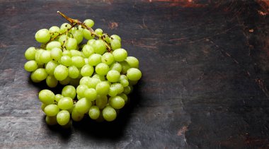 Olgun yeşil üzümlü ve su damlalı bir dal. Tahta arka planda sulu üzümler, yakın plan. Fotokopi alanı olan koyu mutfak masasında üzümler