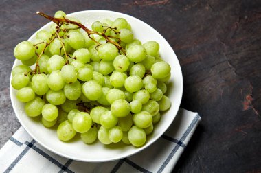 Tabakta su damlaları olan olgun yeşil üzüm dalı. Tahta arka planda sulu üzümler, yakın plan. Fotokopi alanı olan koyu mutfak masasında üzümler